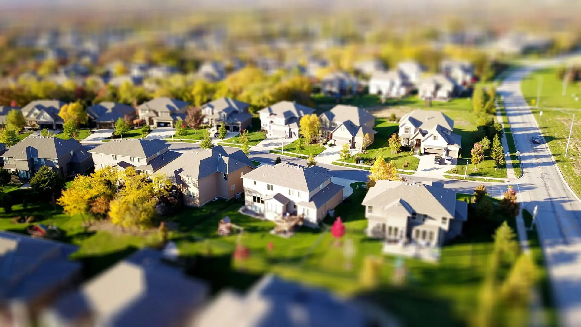 A miniature-style aerial view of a suburban neighborhood with houses and green lawns.