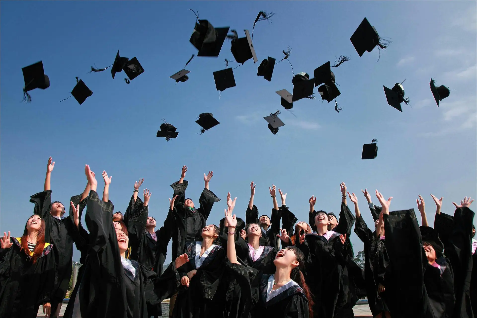 Graduates joyfully toss their caps into a clear blue sky.