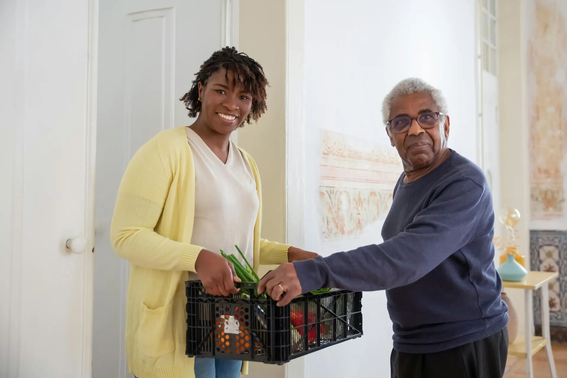 Two smiling people holding a crate of fresh vegetables.