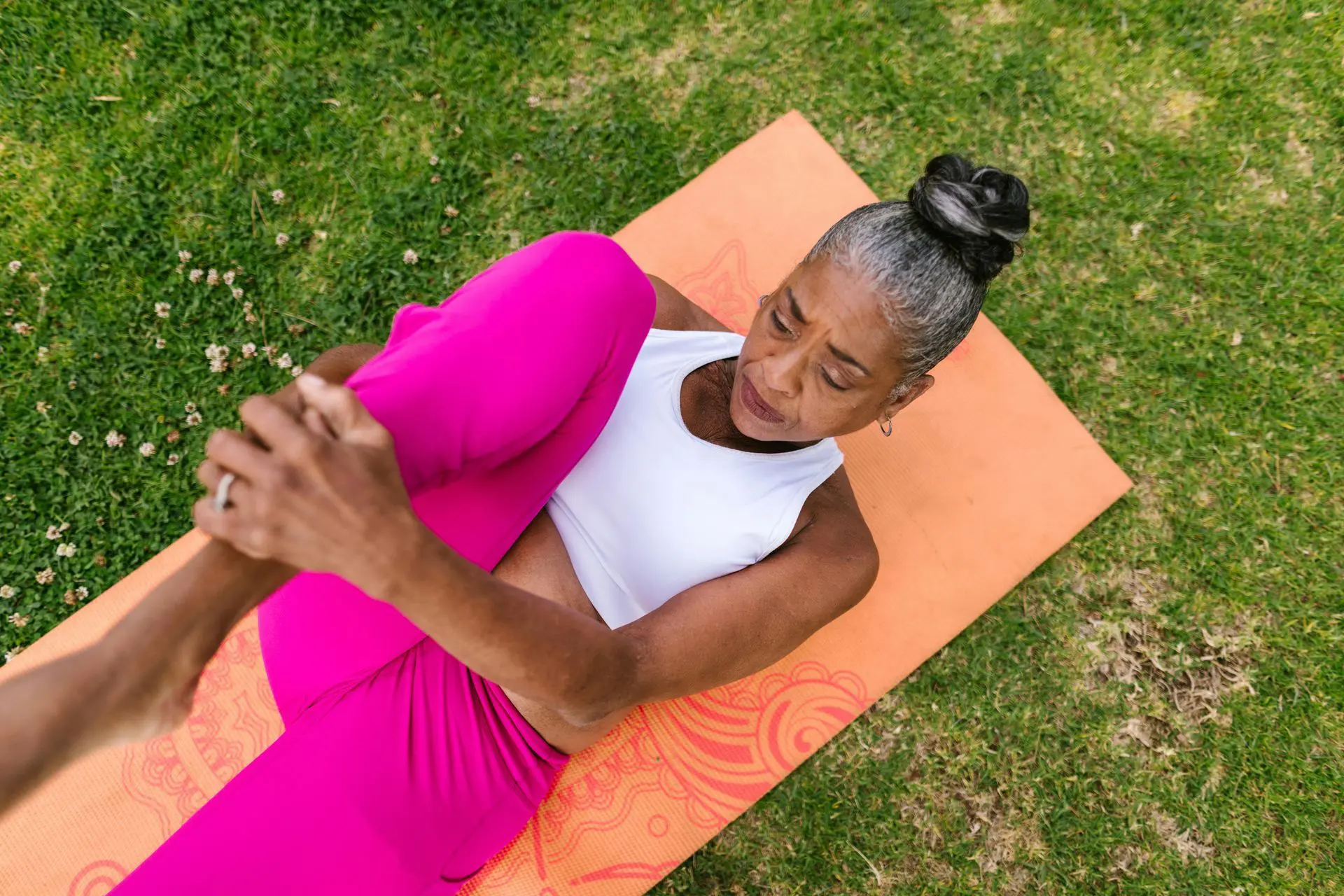Woman stretching on an orange yoga mat outdoors.
