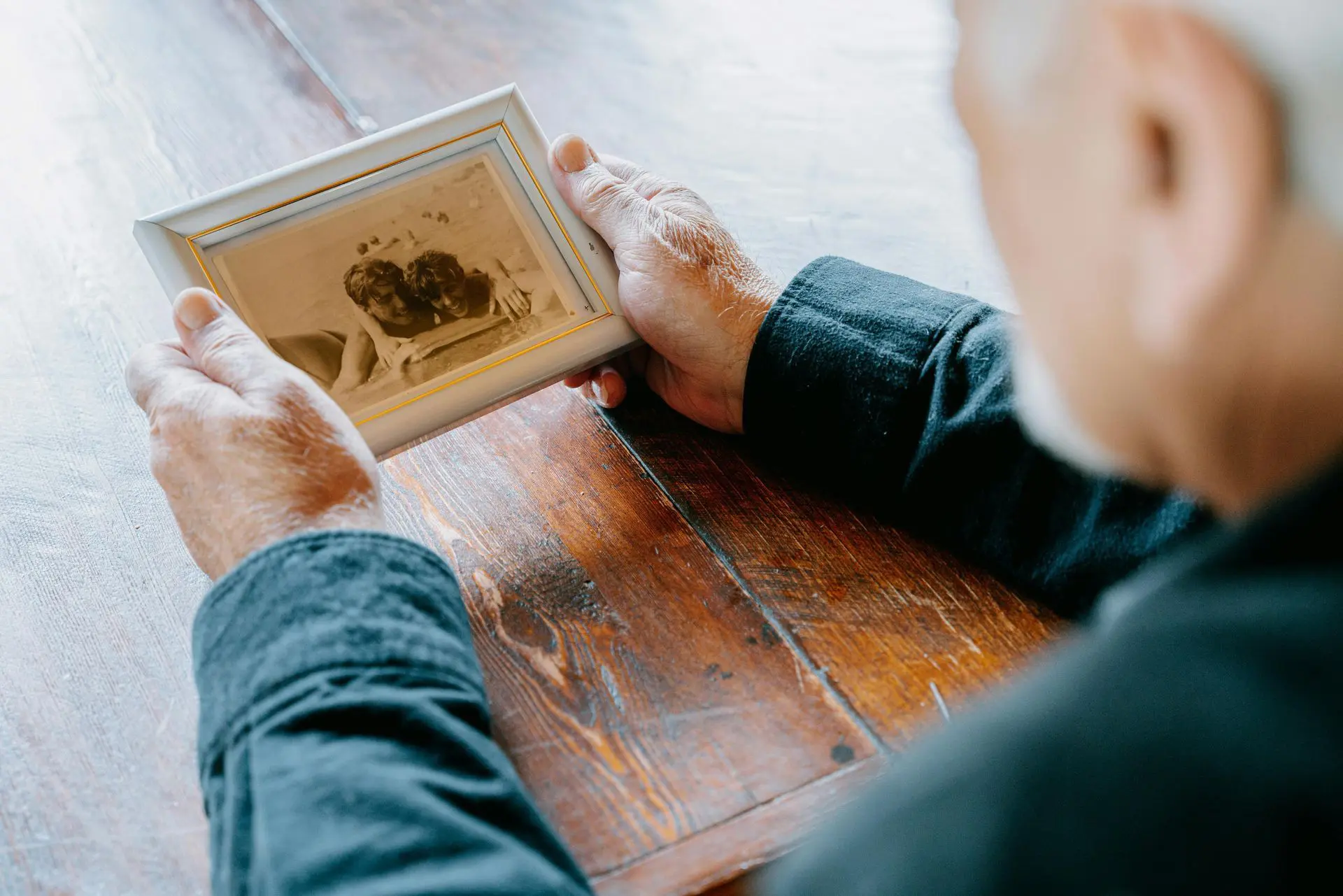 Person holding an old sepia photograph over a wooden table.