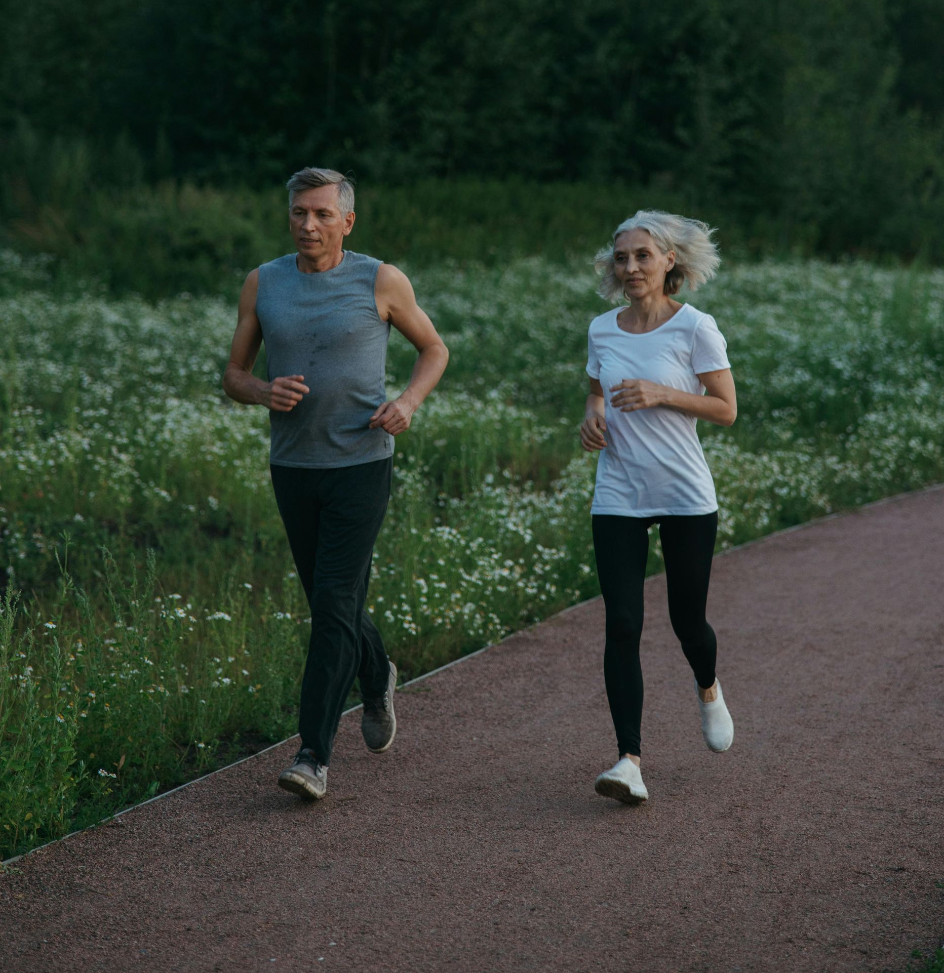 Two women jogging together on a path surrounded by greenery.